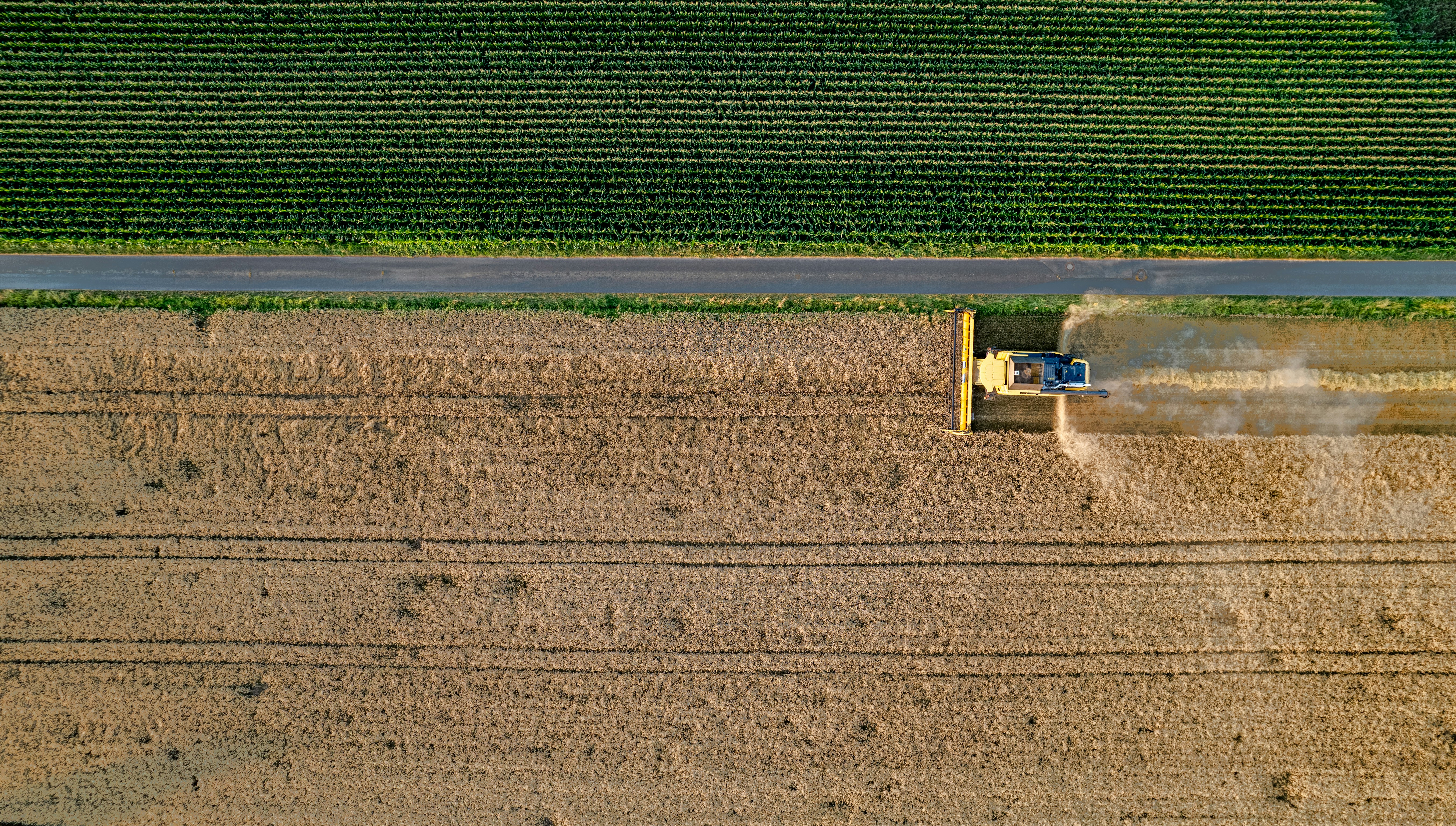 An aerial photo of an agricultural vehicle working in a brown-coloured field, parallel to a green-coloured field