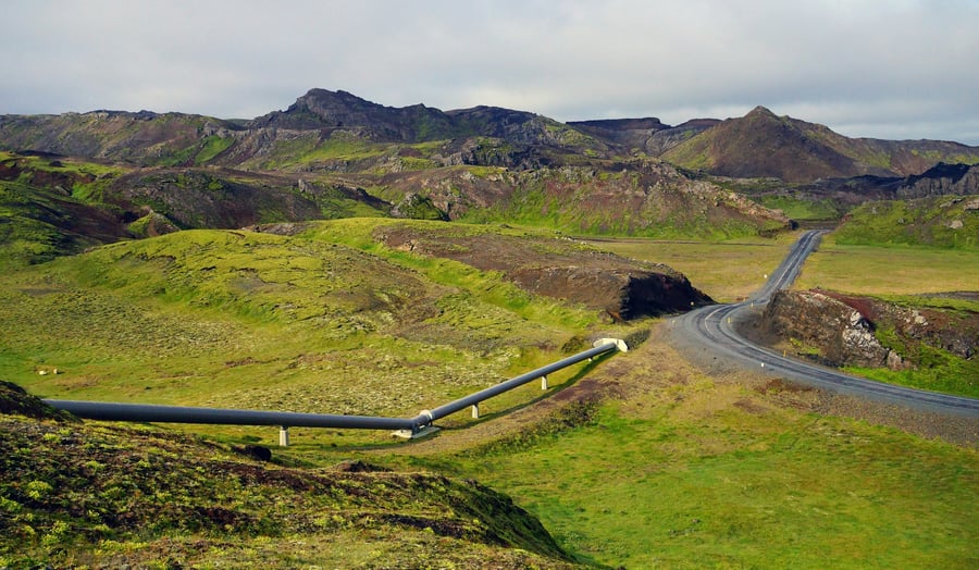 A mountainous, treeless grassy landscape that features a rural road and a pipeline that enters the ground